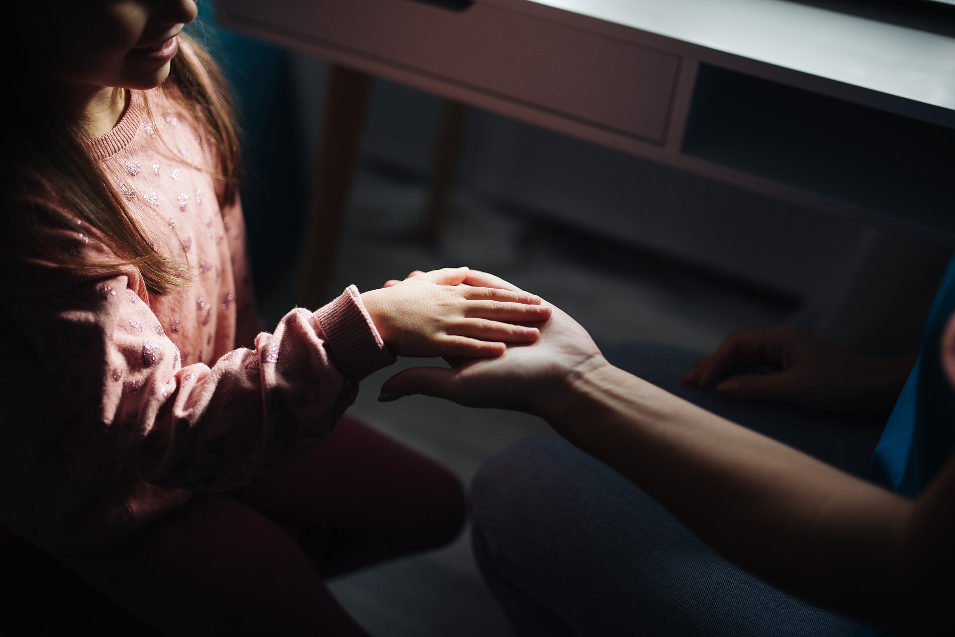 A parent gently holding their child's hand during a quiet moment at home